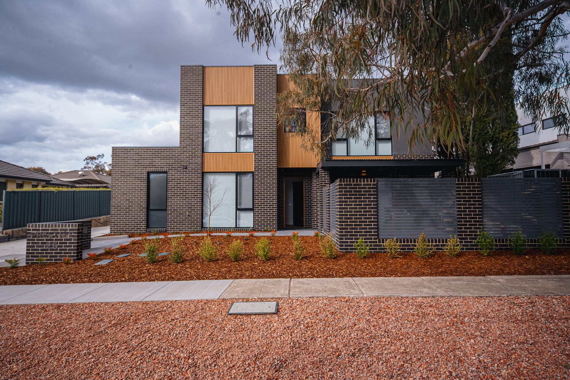 Facade and entry of the Prestige townhouses — charcoal brick with warm timber-look cladding