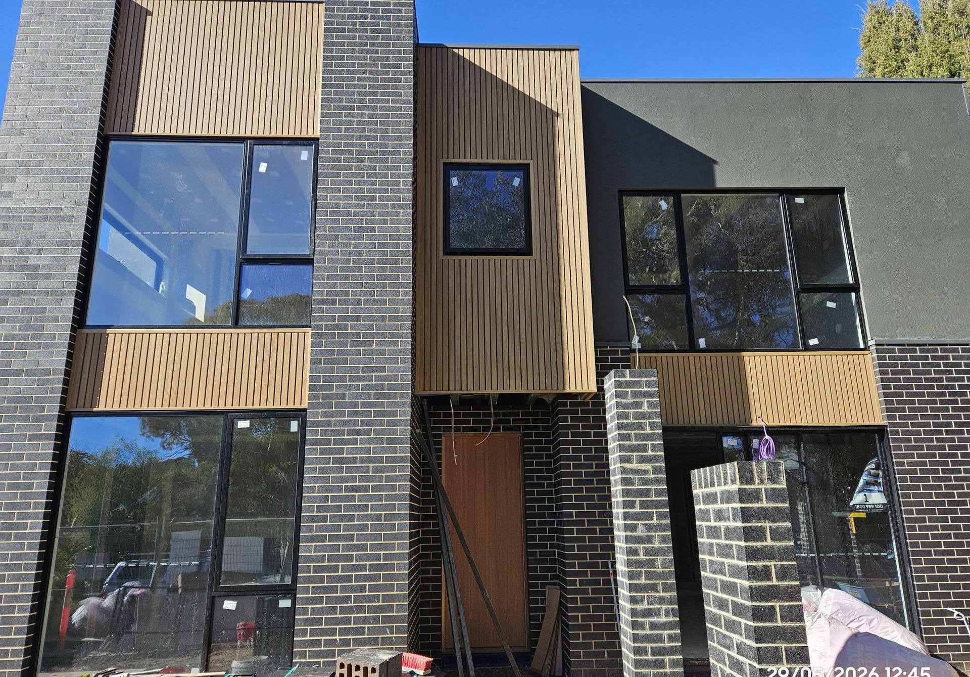 Street facade of the Prestige townhouses — charcoal brick with warm timber-look cladding and full-height glazing